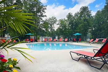A swimming pool with red chaise lounge chairs and umbrellas